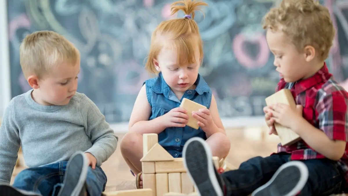 3 kids sharing a wooden building toy