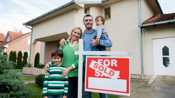 family proudly standing outside their new house