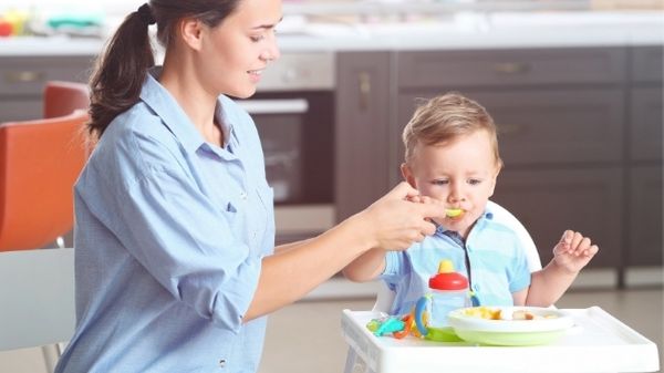 mom feeding toddler in high chair