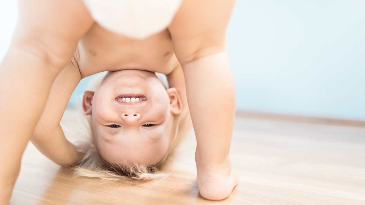 toddler bending over with head on the floor smiling