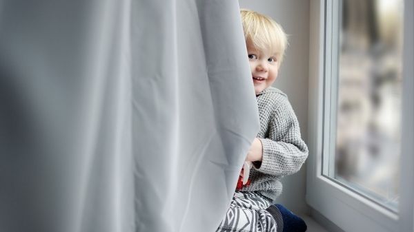 toddler hiding behind curtain smiling