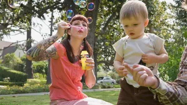 mom blowing bubbles in park with toddler