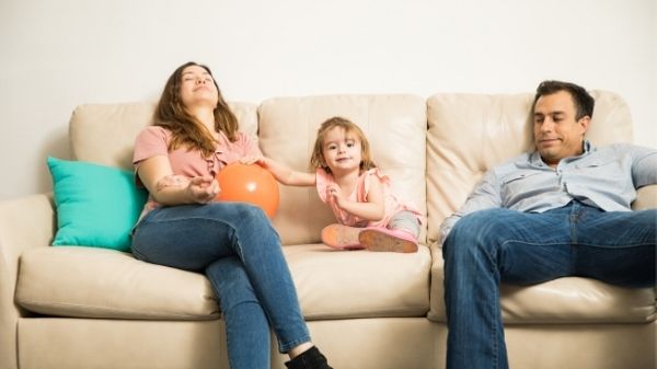 tired mom and dad on sofa with toddler