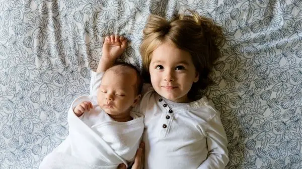 toddler and baby laying on bed