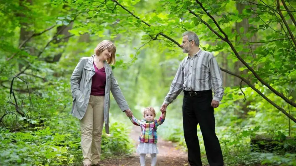 young grandparents walking granddaughter in woodland