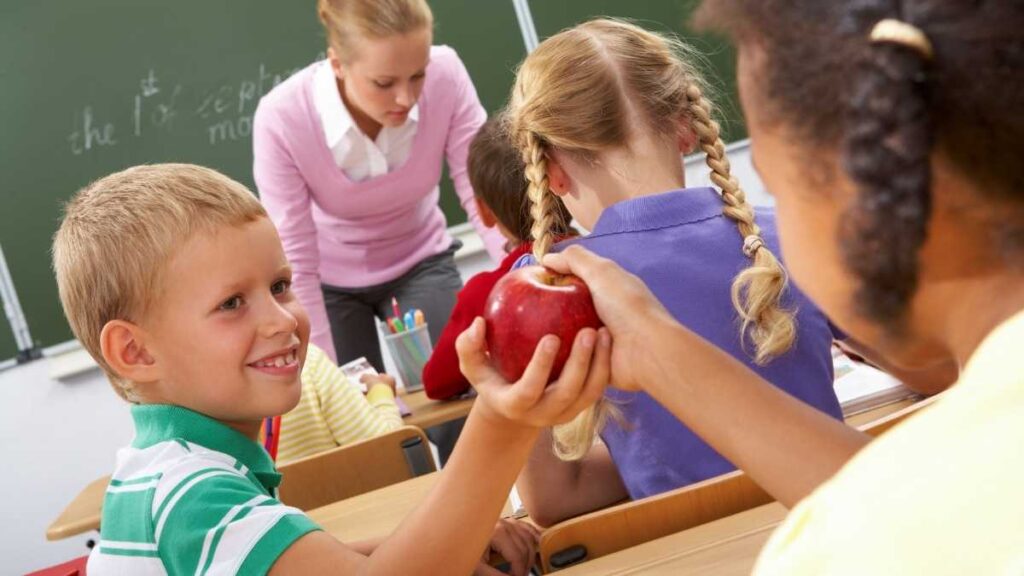 boy handing apple to girl in class