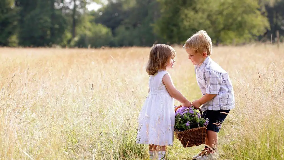 boy helping girl carry a basket of flowers being kind